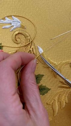 someone is working on something with gold thread and some scissors in front of the fabric