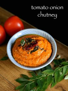 a bowl filled with carrot hummus next to two tomatoes on top of a wooden table