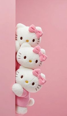 three hello kitty stuffed animals hanging from the side of a pink wall