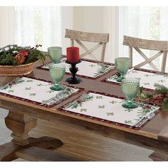 a wooden table topped with green glass dishes and place mats next to a basket filled with flowers