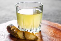 a glass filled with liquid sitting on top of a wooden table next to a sliced cucumber