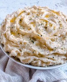 mashed potatoes in a white bowl with herbs on top and seasoning sprinkled on the side