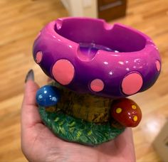 a purple mushroom shaped candle holder sitting on top of a wooden stump next to a person's hand