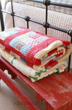 three quilts are stacked on top of a red bench in front of a bed