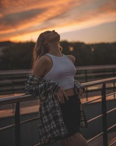 a woman standing on a bridge looking up at the sky with her hands in her pockets