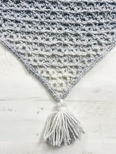 a crocheted triangle with a tassel on the side and a white fringe hanging from it