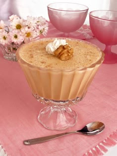 there is a dessert in the glass bowl on the table with pink flowers and other dishes behind it