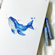 two blue markers are next to a white card with a drawing of a whale on it