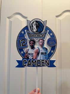 a person holding up a stick with the image of two basketball players on it in front of a door