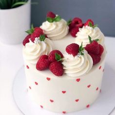 a white cake with raspberries and cream frosting on top sitting on a plate