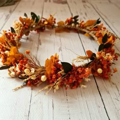 a wreath made out of dried flowers and leaves on a white wooden floor with an orange flower arrangement in the middle