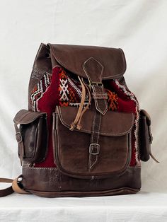 Handmade Moroccan Leather and Rug Backpack | Artisan Made Rucksack Medium Backpack/Rucksack - this bag is made with dyed brown coloured leather and a gorgeous red kilim rug. Includes 2 inside pockets, and 4 outside pockets. Brought to you from the souks of Marrakech, we are a mixed Moroccan-British family run business who personally hand picked all of our artisan made products to bring them to London. We value quality craftsmanship as well as fair pay and conditions to all of our suppliers, whic Souk Marrakech, Red Kilim Rug, Recycled Rugs, British Family, Larp Armor, Red Leather Bag, Moroccan Leather, Medium Backpack, Colored Leather