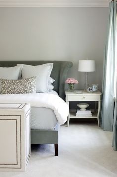 a white bed sitting in a bedroom next to a window with curtains on the windowsill