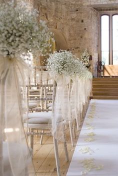 the aisle is decorated with white flowers and ribbon as well as chairs for guests to sit in