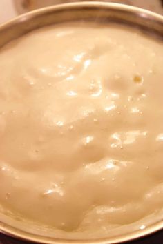 a metal bowl filled with white sauce on top of a table next to a knife