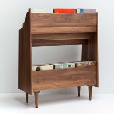 a wooden book shelf with magazines on it's bottom and two drawers below the shelves