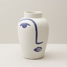 a white vase with blue lines on it and a face painted on the front side