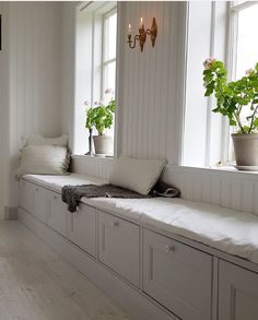 a white room with some plants in the window sill and pillows on the bench