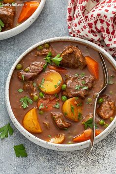 two bowls of beef stew with carrots, potatoes and parsley on the side