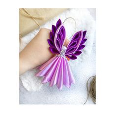 a woman's hand holding a purple flower shaped ornament on top of a white blanket