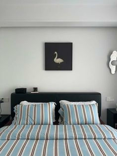 a bed with blue and white striped sheets in a bedroom next to a painting on the wall