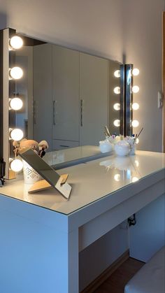 a vanity with lights on it and a bowl of flowers in front of the mirror