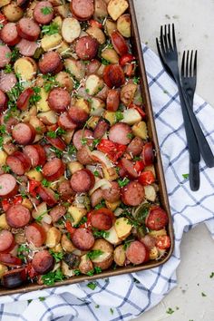 a pan filled with sausage and potatoes on top of a table next to two forks