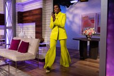 a woman standing in front of a couch wearing a bright yellow suit and matching heels