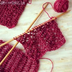 two crocheted pieces of red yarn with wooden knitting needles on the floor next to them