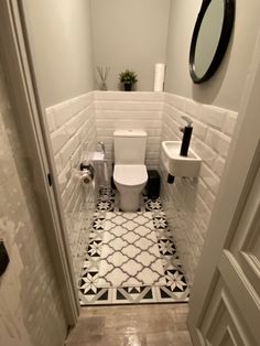 a white toilet sitting inside of a bathroom next to a sink under a round mirror