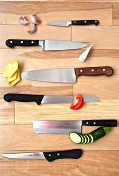 several knives are lined up next to each other on a wooden surface with sliced vegetables