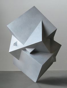 an abstract sculpture is displayed on the floor in front of a white wall and grey background