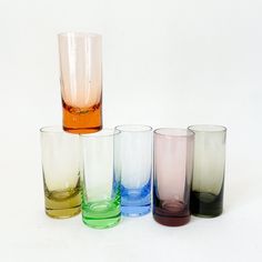 five different colored glasses sitting next to each other on a white surface, with one empty glass in the middle