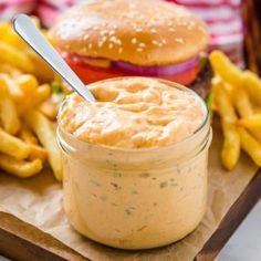 a sandwich and french fries on a wooden tray with a jar of sauce next to it