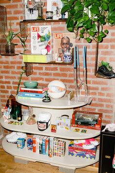 a shelf with books, magazines and other items on it in front of a brick wall