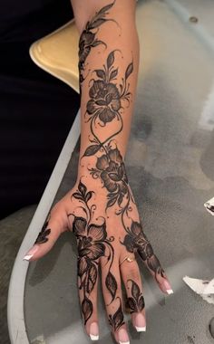 a woman's hand with tattoos on it and flowers on her arm, sitting at a table