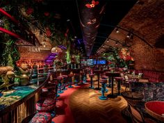 the inside of a restaurant with many tables and stools, plants on the walls