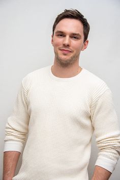 a man standing in front of a white wall with his hands in his pockets and looking at the camera