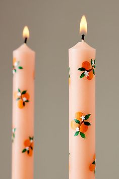 two candles with oranges painted on them sitting side by side in front of each other