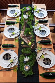 the table is set with white plates and silverware, green moss growing on it