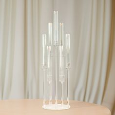 four clear vases sitting on top of a wooden table next to a white curtain