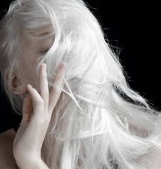 a woman with long white hair holding her hand to her face