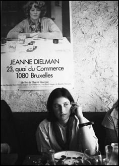 a woman sitting at a table in front of a poster