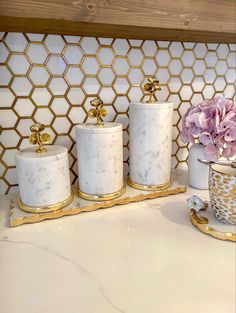 three white marble canisters with gold accents and flowers in them on a counter