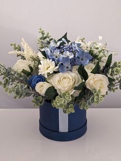 a blue and white flower arrangement in a round container on a table with grey background