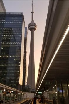 a train station with people walking on the platform and two tall buildings in the background