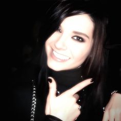 a woman with long black hair and piercings making the v sign while smiling at the camera