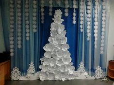 a christmas tree made out of paper plates and snowflakes is displayed in front of a blue curtain