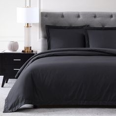 a bed with black comforter and pillows in a white room next to a night stand