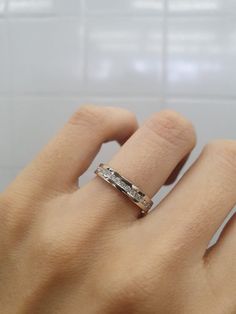 a woman's hand with a wedding ring on top of her finger, in front of a tiled wall